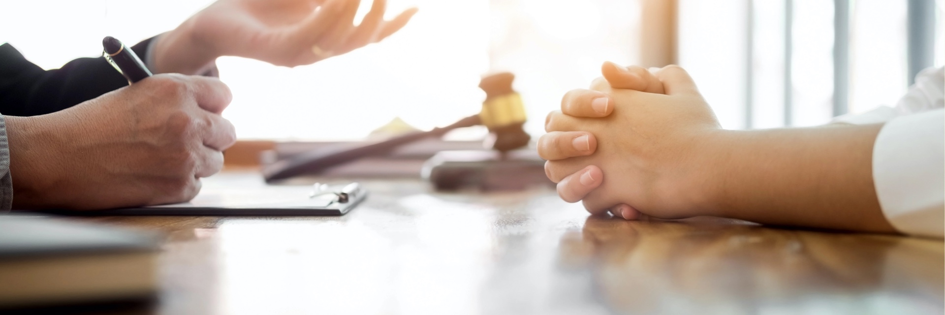 Consultation entre un avocat criminel et son client, mettant en avant des mains jointes et un marteau de juge en arrière-plan, symbolisant le conseil juridique en matière de droit pénal.