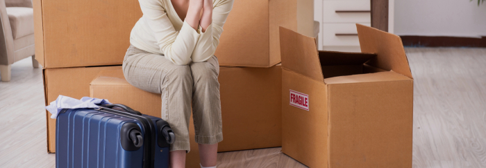 Femme bouleversée assise parmi des boîtes de déménagement et une valise après une rupture, contexte possible de harcèlement criminel.